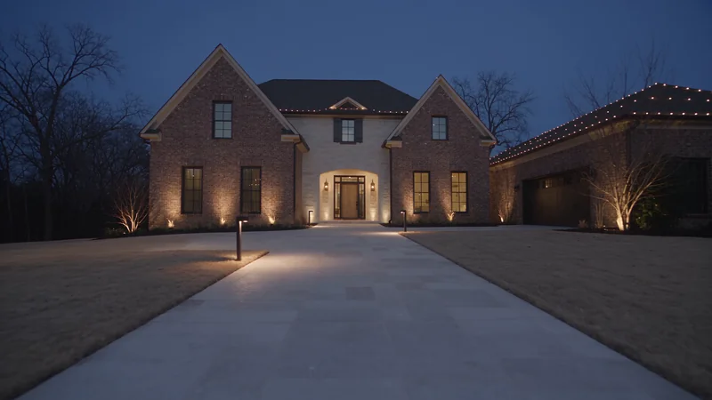 A limestone pathway lit by bronze fixtures leads toward a warm timber entrance at dusk.
